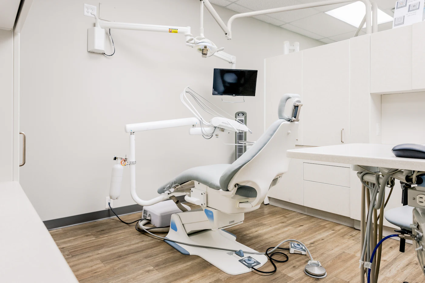 Inside the clinic: a bright treatment room with a white dental chair and a desk