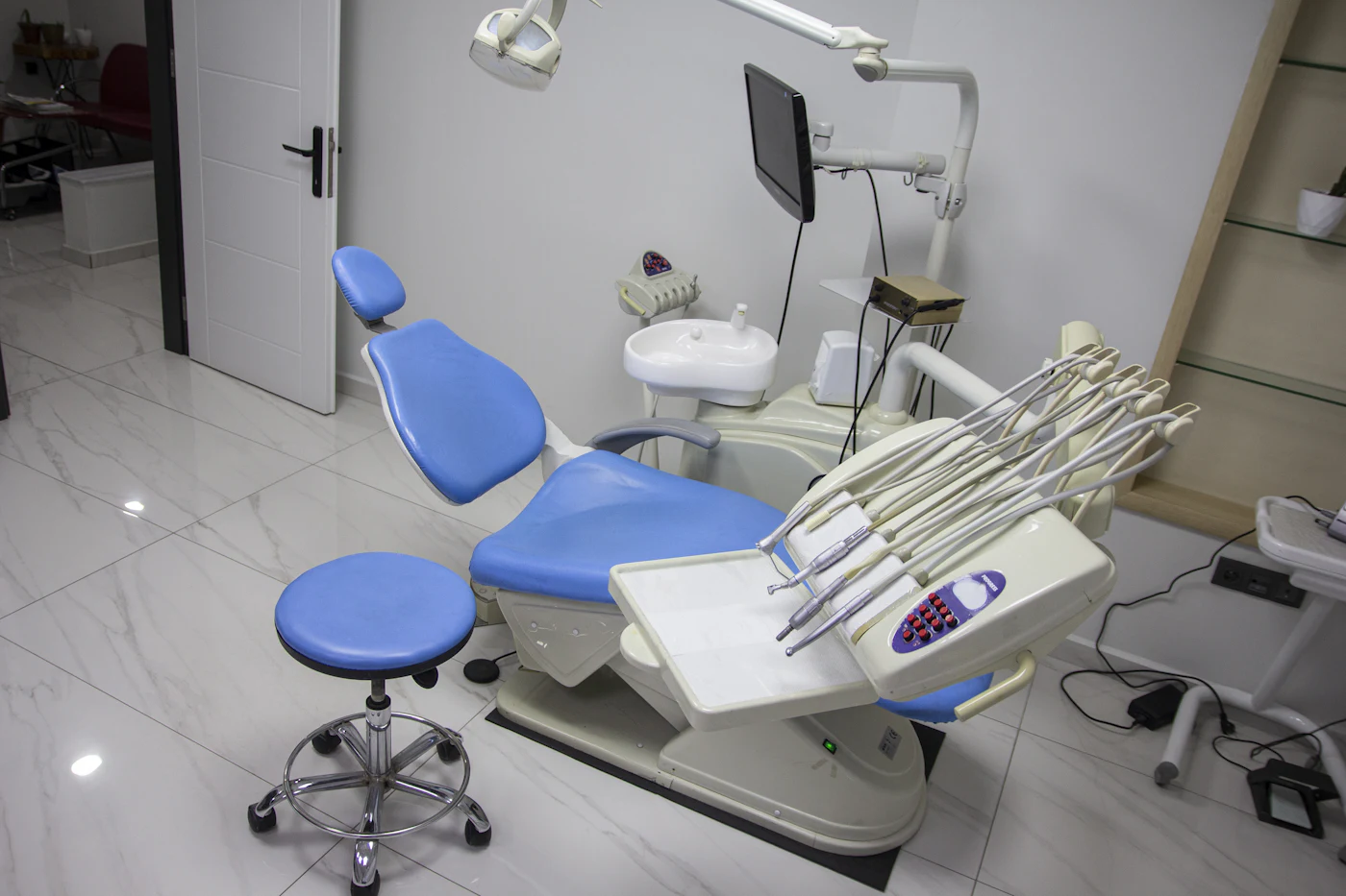 A clean treatment room with a blue dental chair and instrument tray