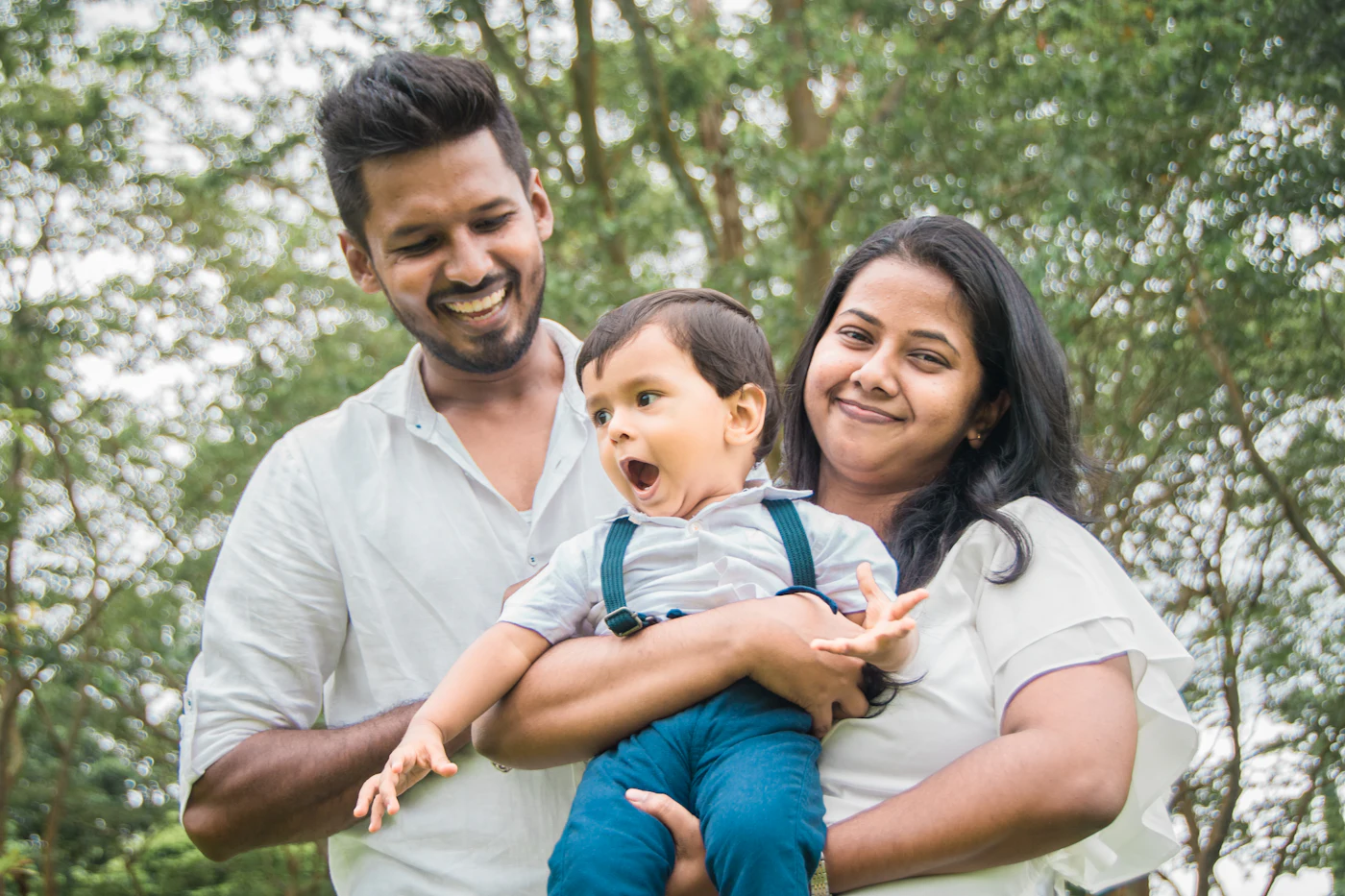 A smiling young couple holding their toddler son outdoors