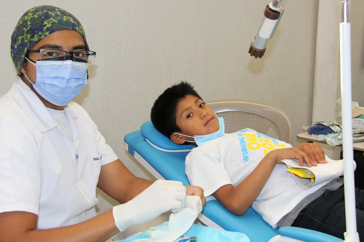 A young boy lying back in a blue dental chair while the dentist gets ready to check his teeth