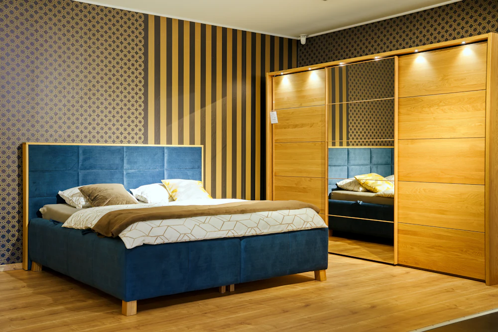 A king size cot with a padded headboard next to a wooden sliding wardrobe