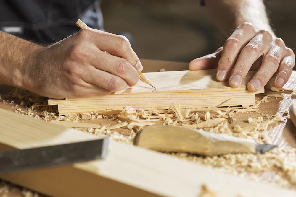 A carpenter marking a cutting line on a plank with a pencil