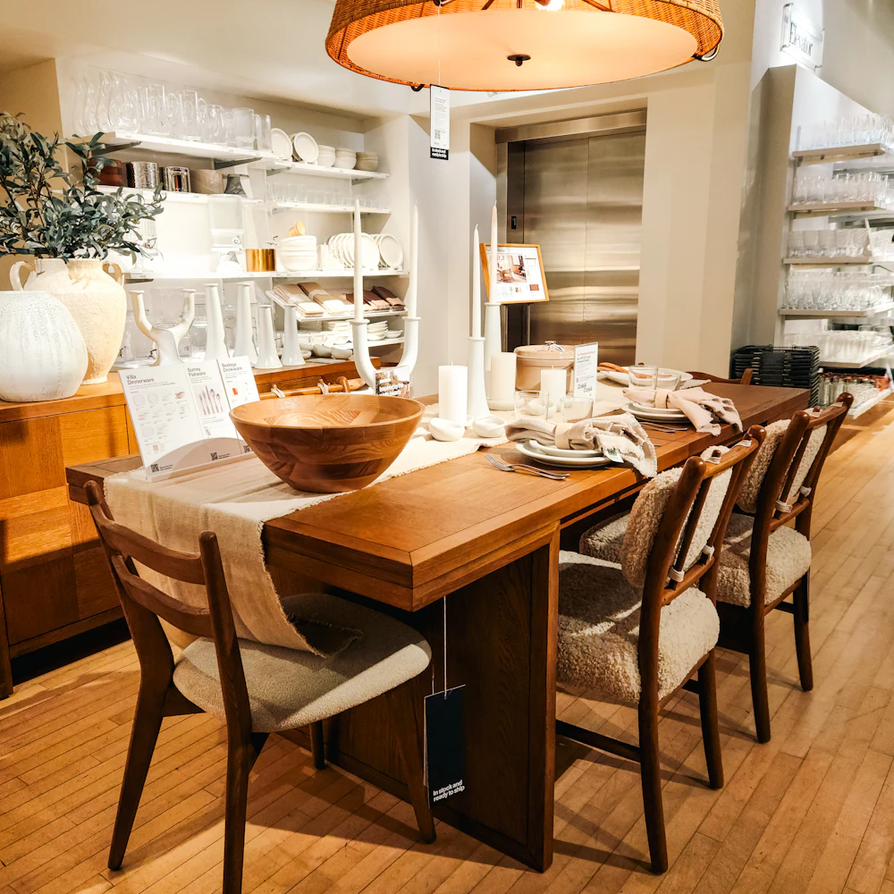 A six-seater solid wood dining table with matching chairs under a cane lamp