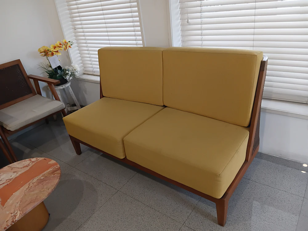 A mustard two-seater sofa on a solid wood frame by a window