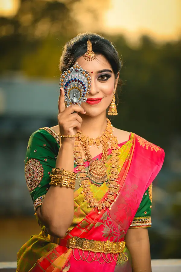 A bride in a green and pink silk saree and gold jewellery, smiling