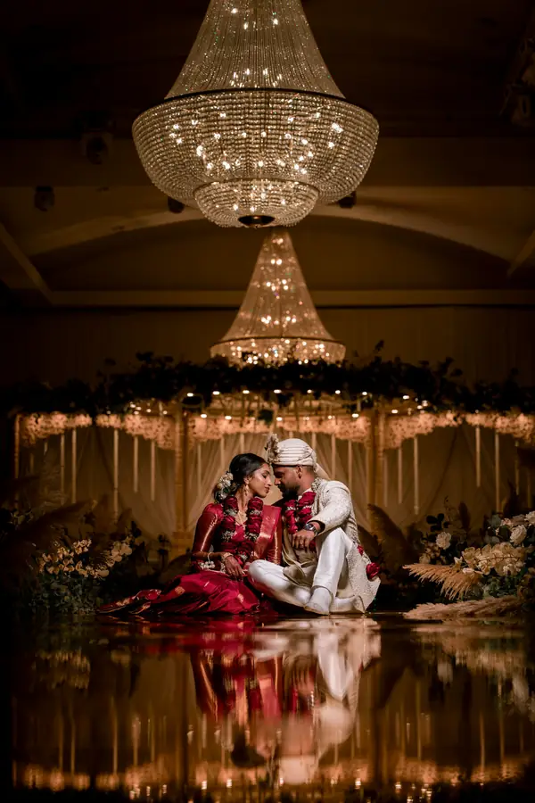 Bride and groom seated under two crystal chandeliers, the stage lights reflected in a glossy floor