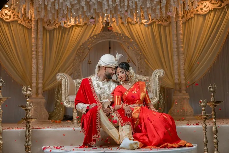 Bride and groom in red silk on the reception stage, with tall brass lamps on both sides