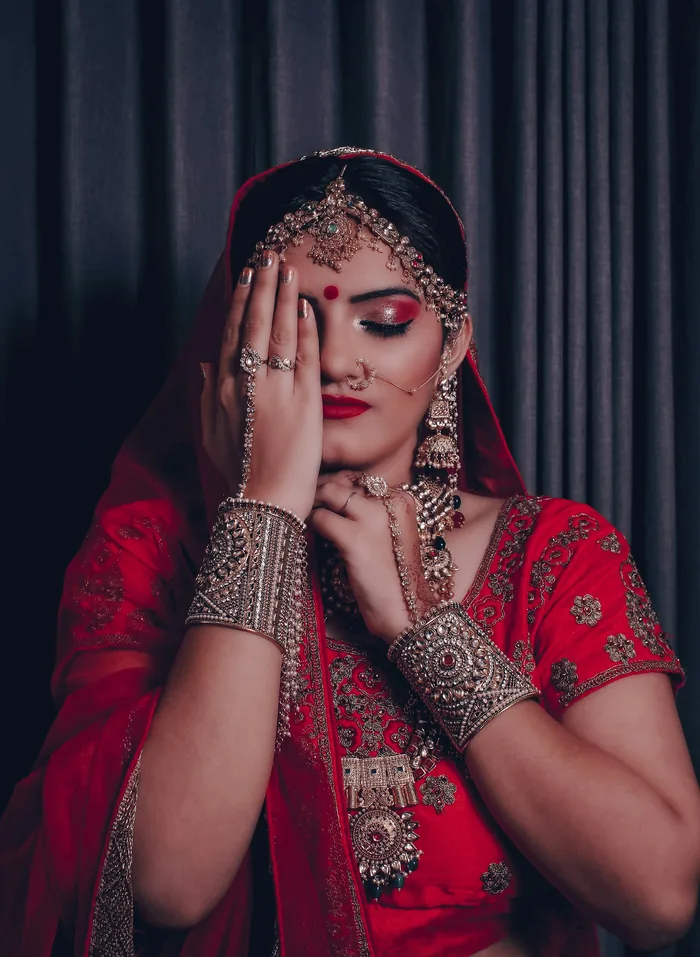 Bride in red with gold jewellery and a mehendi hand covering one eye
