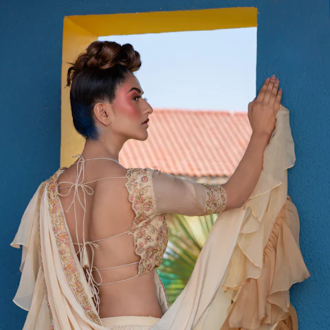Woman holding out the pallu of a cream saree by a blue wall