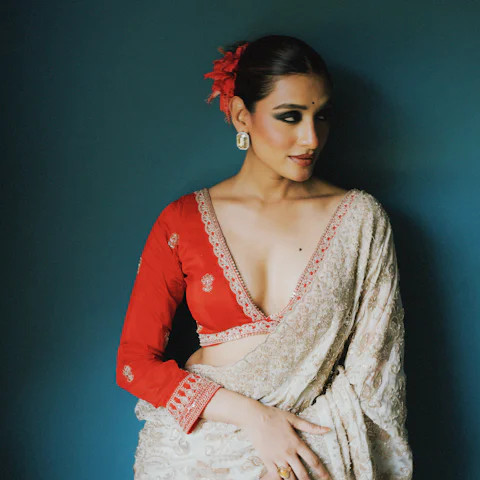Red blouse with a white embroidered saree against a teal wall