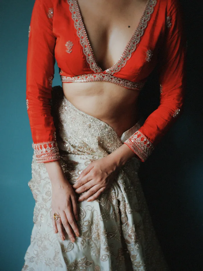 Close view of a red blouse with a deep V neck and gold aari embroidery on the neckline and sleeves