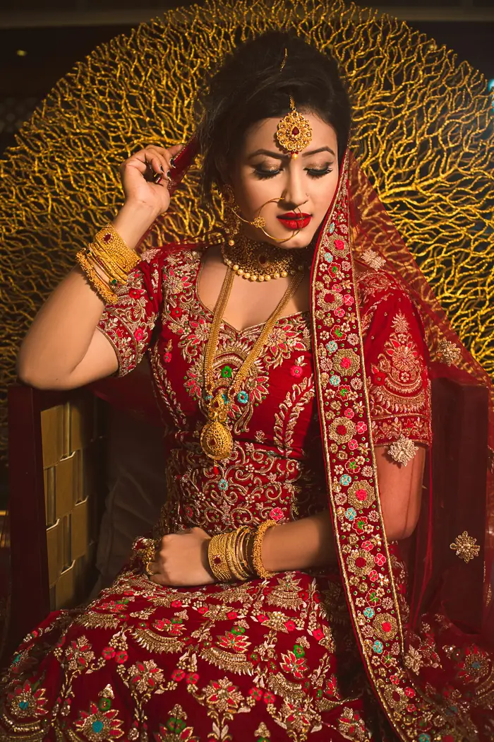 Bride in a red and gold embroidered blouse and lehenga, seated against a gold backdrop